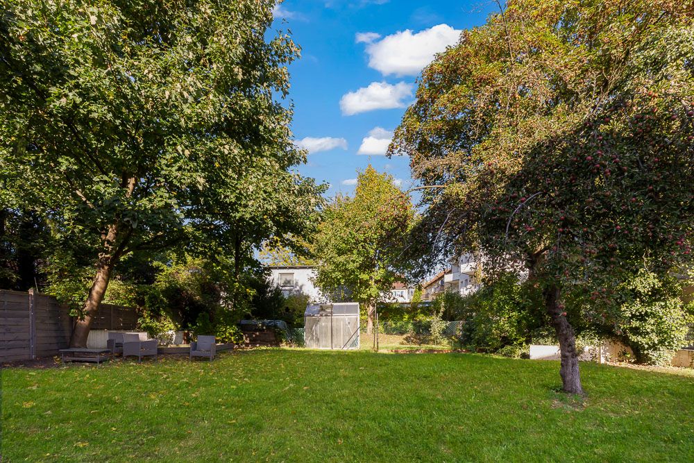 Großer Garten mit grünem Rasen, Bäumen und Gartenmöbeln im Schatten.
