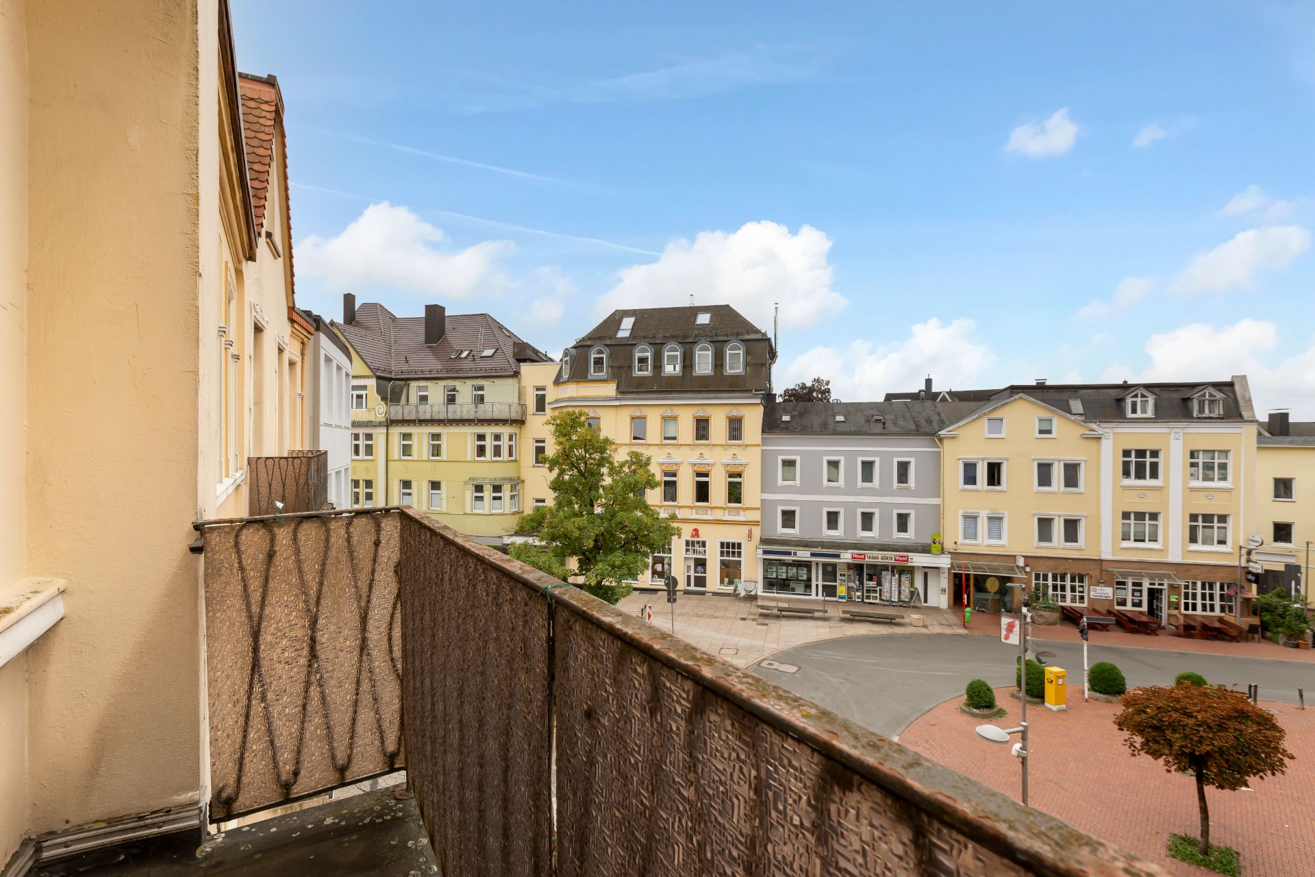 Blick von einem Balkon auf einen kleinen Platz mit mehreren mehrstöckigen Wohnhäusern.