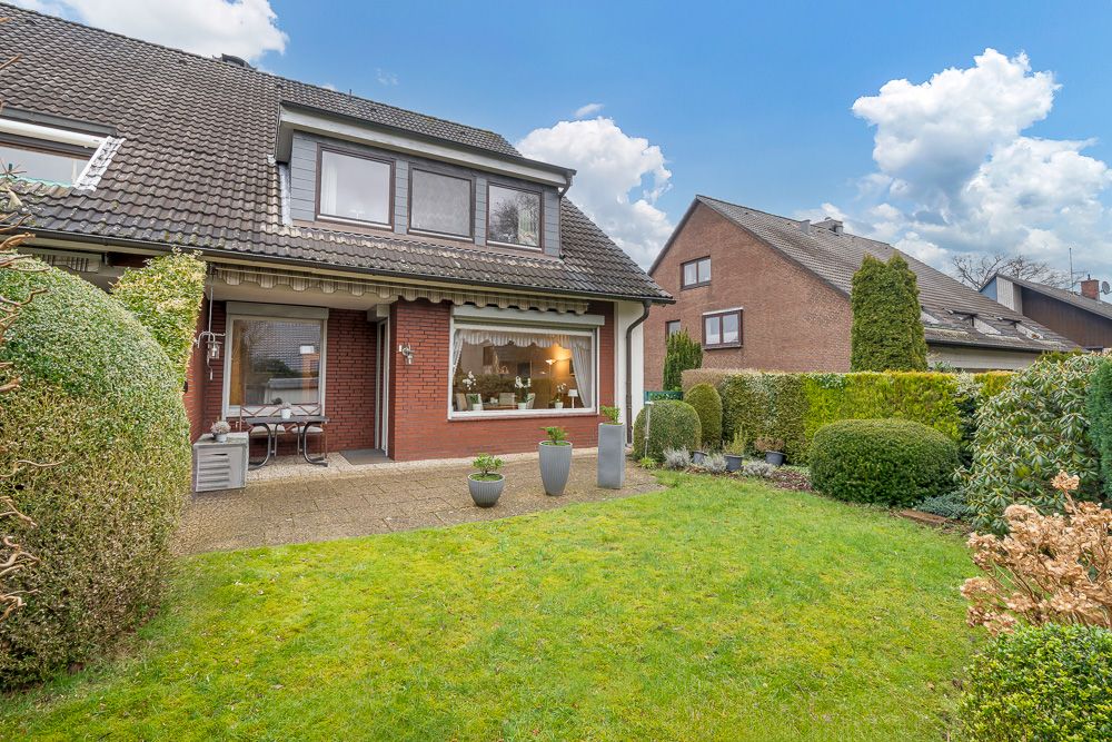 Gepflegter Garten mit Terrasse vor einem roten Wohnhaus mit großen Fenstern.