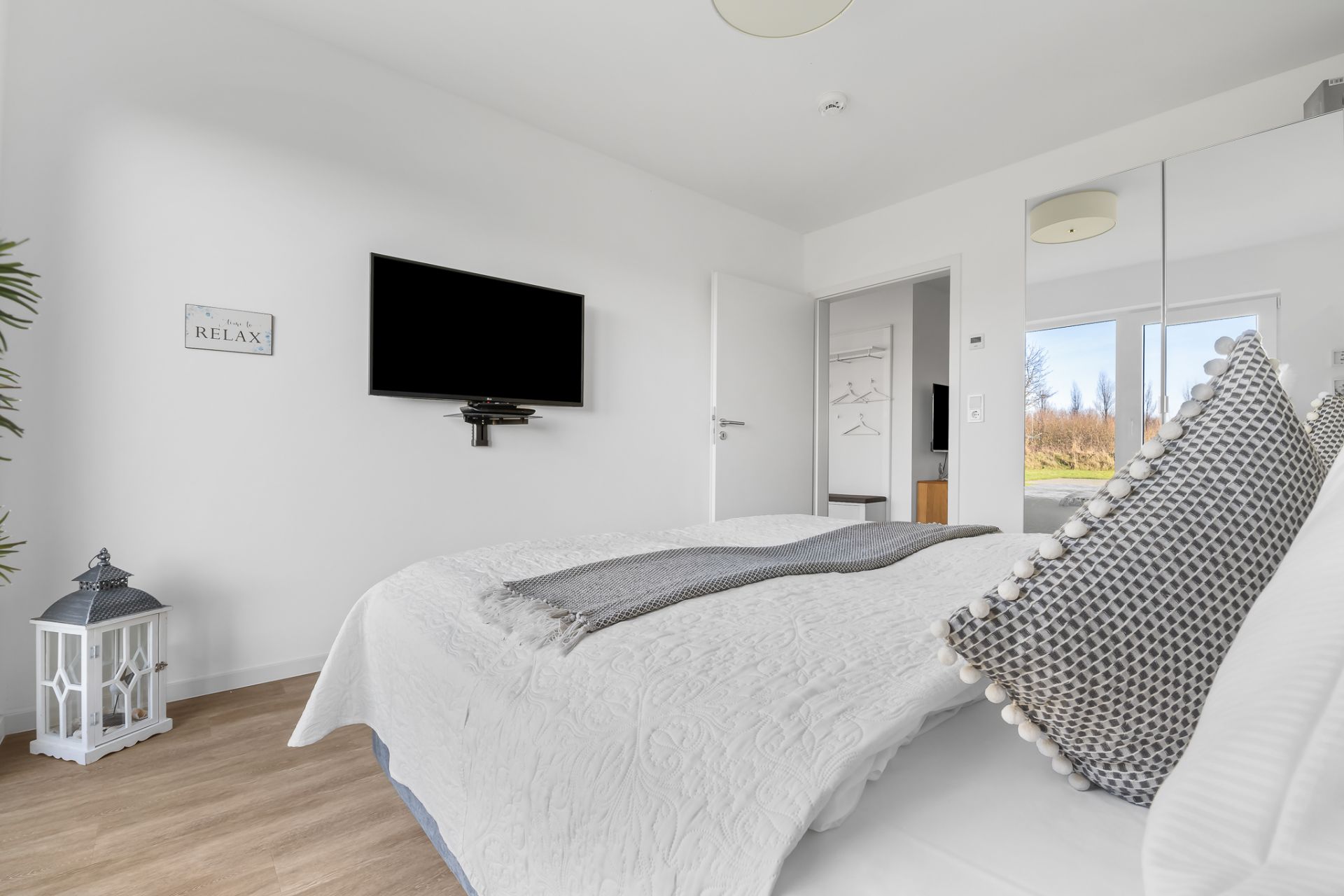Helles Schlafzimmer mit Doppelbett, TV an der Wand und Spiegel-Schrank.
