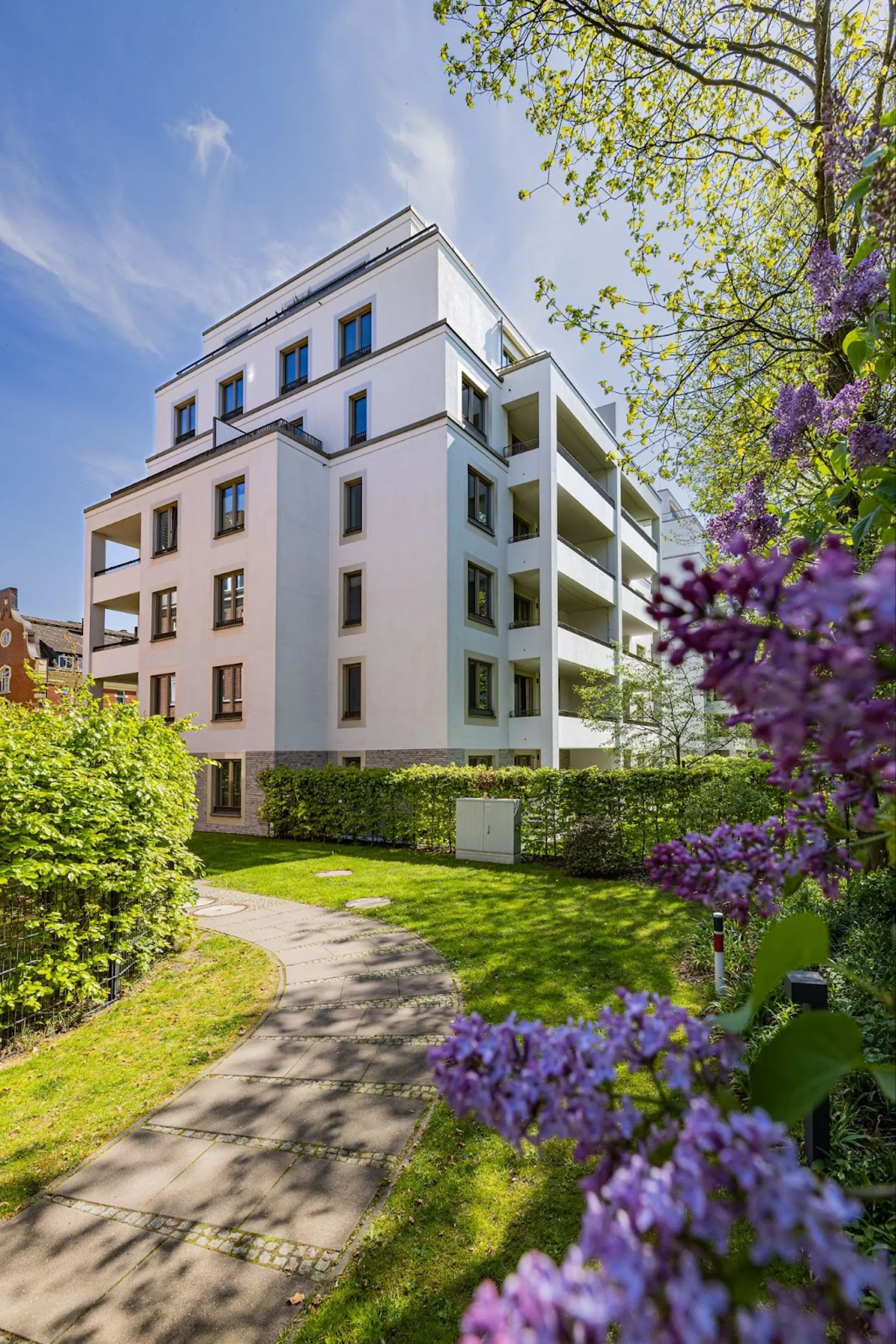 Modernes Wohnhaus mit mehreren Etagen, umgeben von Garten, Blumen und einem Gehweg.