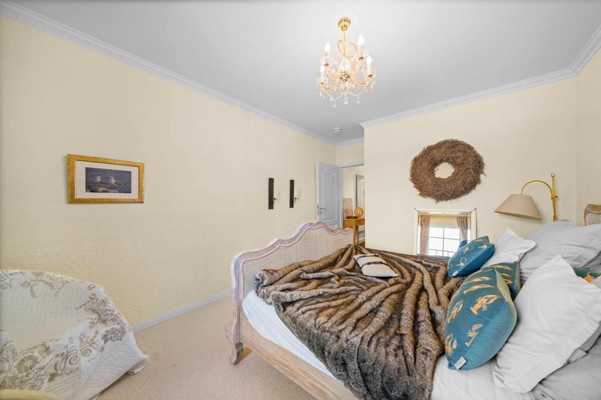Schlafzimmer mit Bett, Kissen, Decke, Kronleuchter und Dekoration an den Wänden.