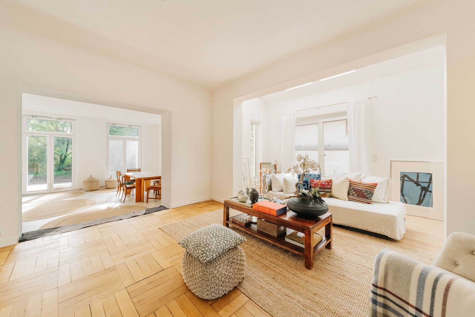 Helles Wohnzimmer mit Holzboden, Sofa, Couchtisch und Essbereich im Hintergrund.
