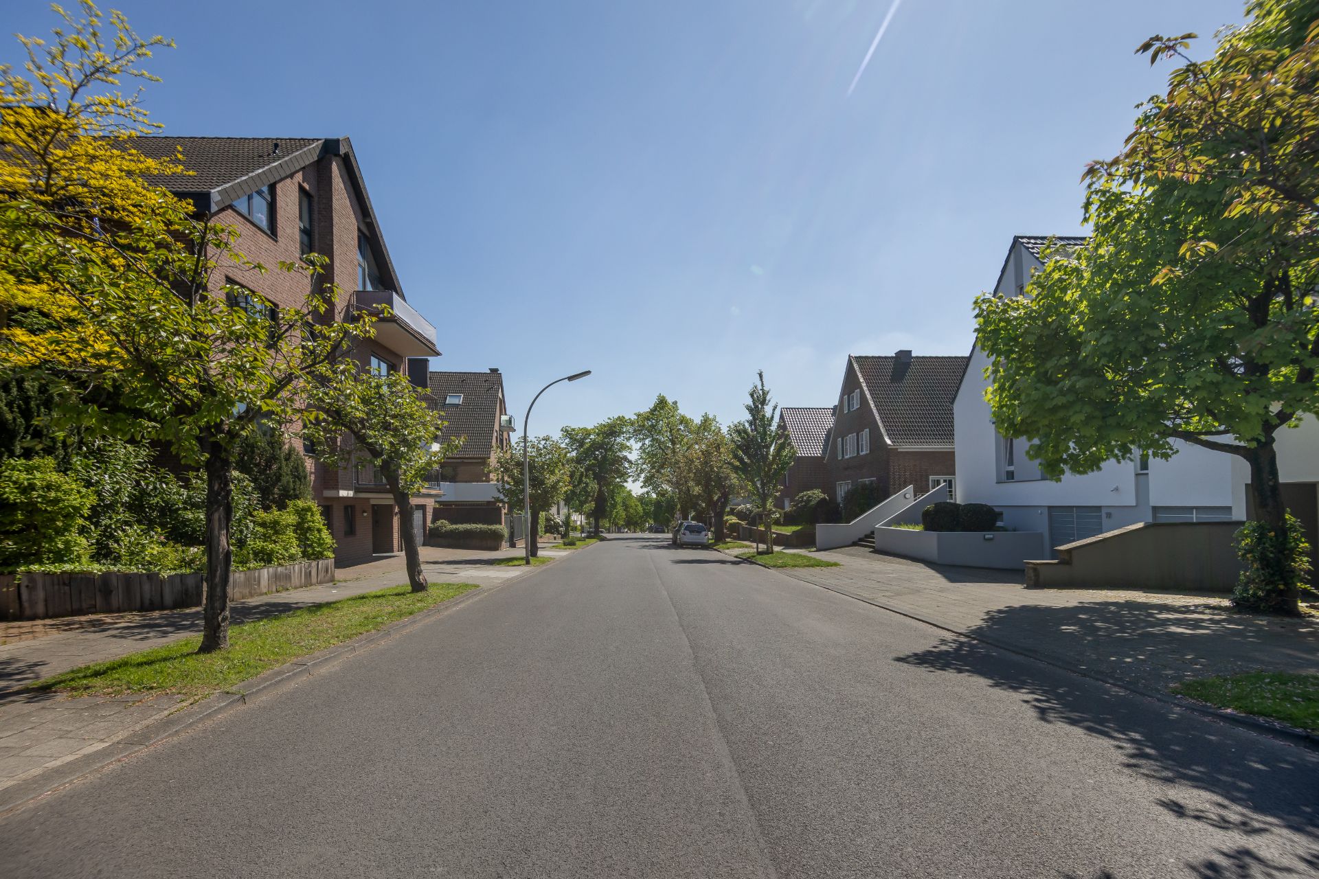 Ruhige Wohnstraße mit Einfamilienhäusern, Bäumen und Gehwegen bei sonnigem Wetter.