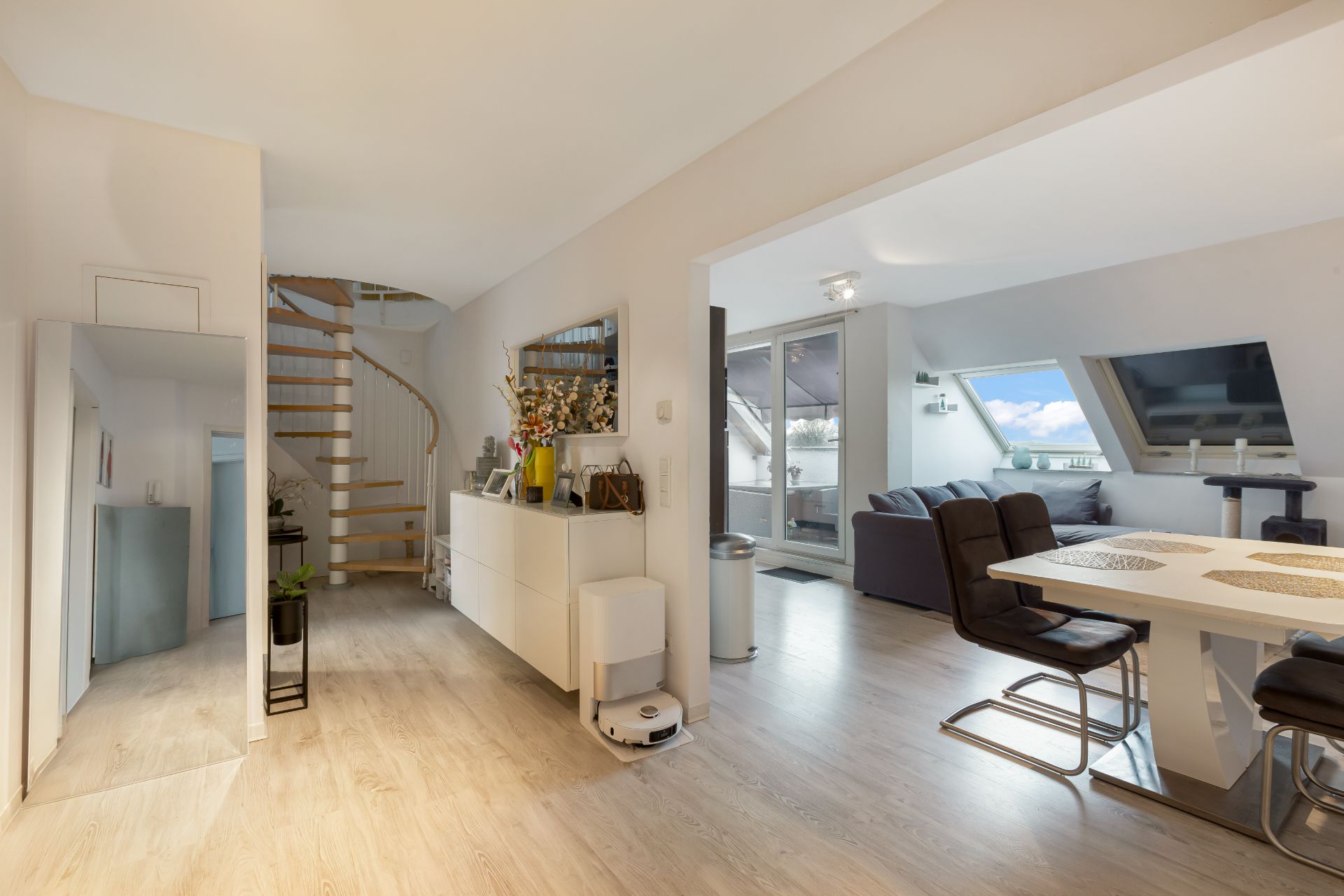 Helles Wohnzimmer mit Esstisch, Stühlen, Sofa und Treppe in einer modernen Wohnung.