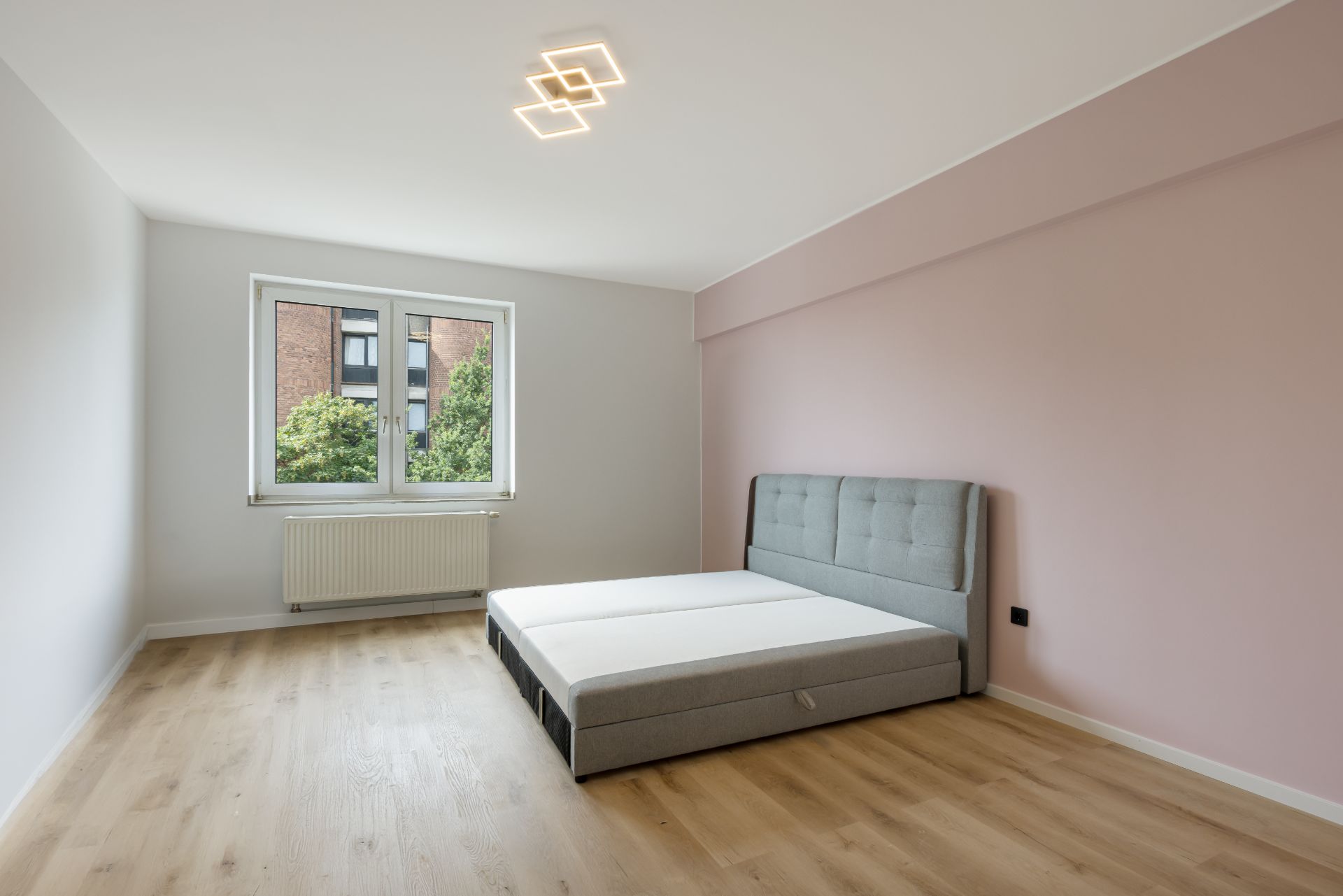 Helles Schlafzimmer mit Doppelbett, Holzfußboden und Fenster mit Blick ins Grüne.