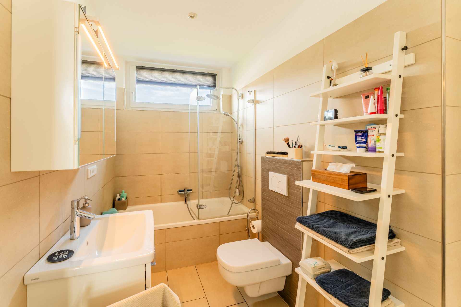 Modernes Badezimmer mit Badewanne, Toilette, Waschbecken und Regal mit Handtüchern.
