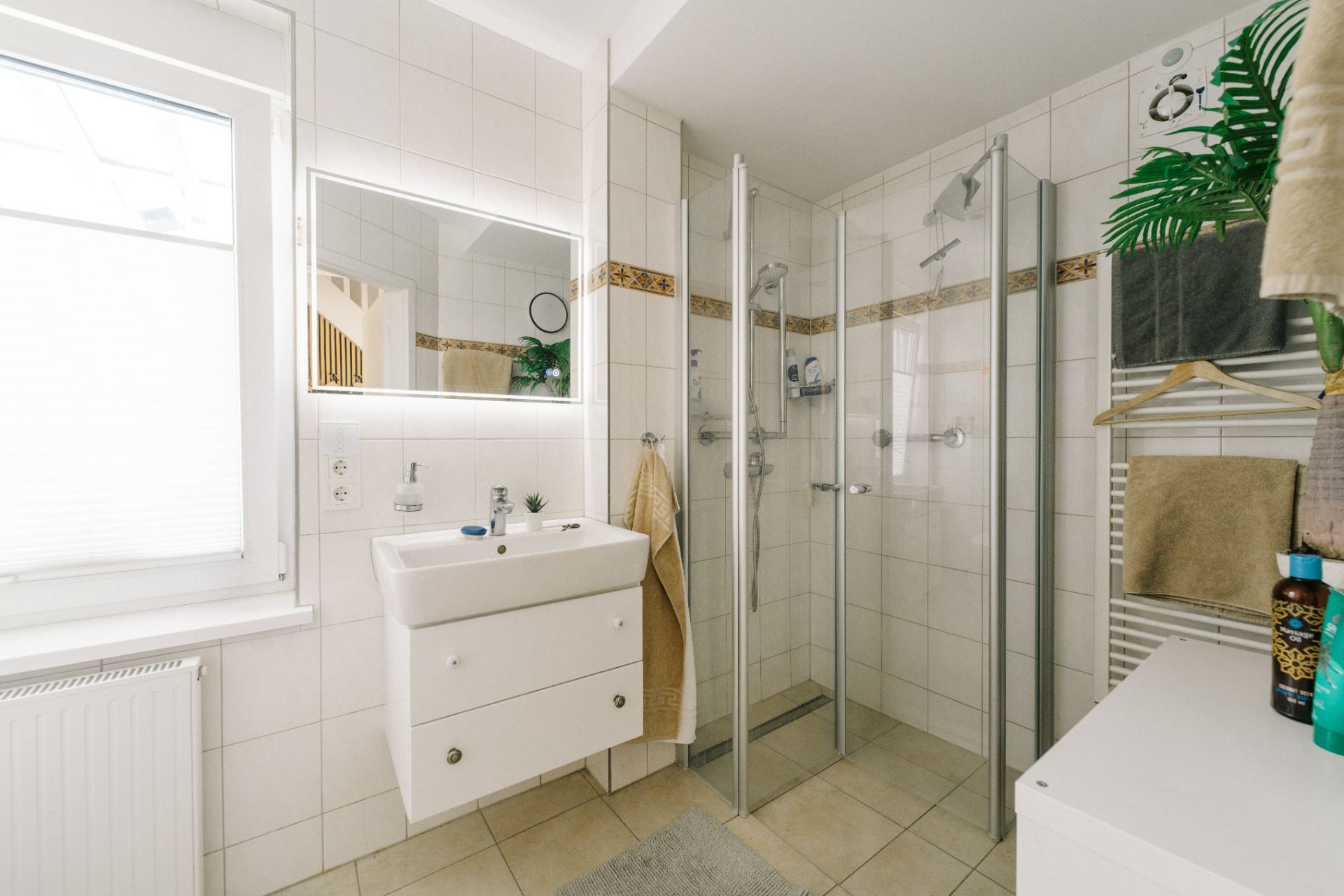 Modernes Badezimmer mit Dusche, Waschbecken, großem Spiegel und Handtüchern an der Wand.