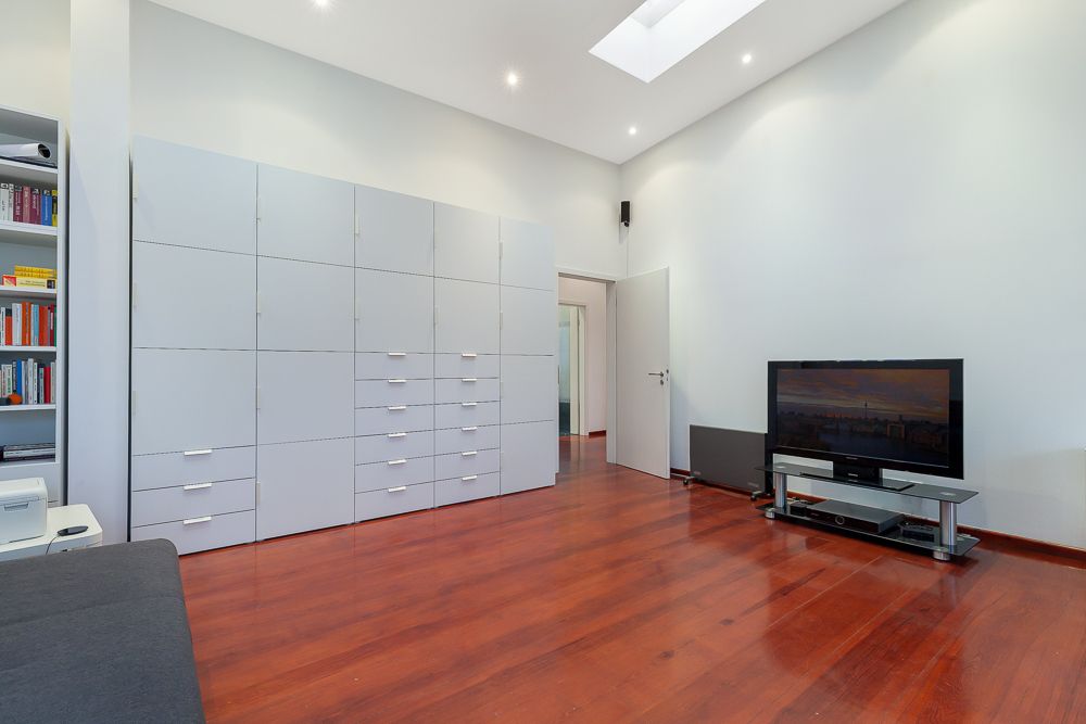 Wohnzimmer mit Holzboden, großem weißen Schrank, Fernseher und Bücherregal.