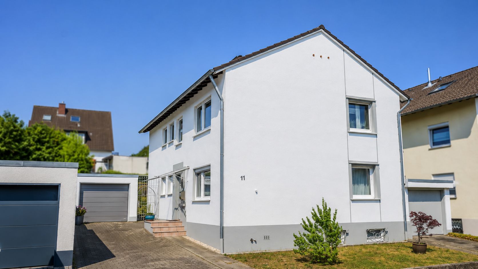 Weißes Einfamilienhaus mit Vorgarten und Garage an einem sonnigen Tag.