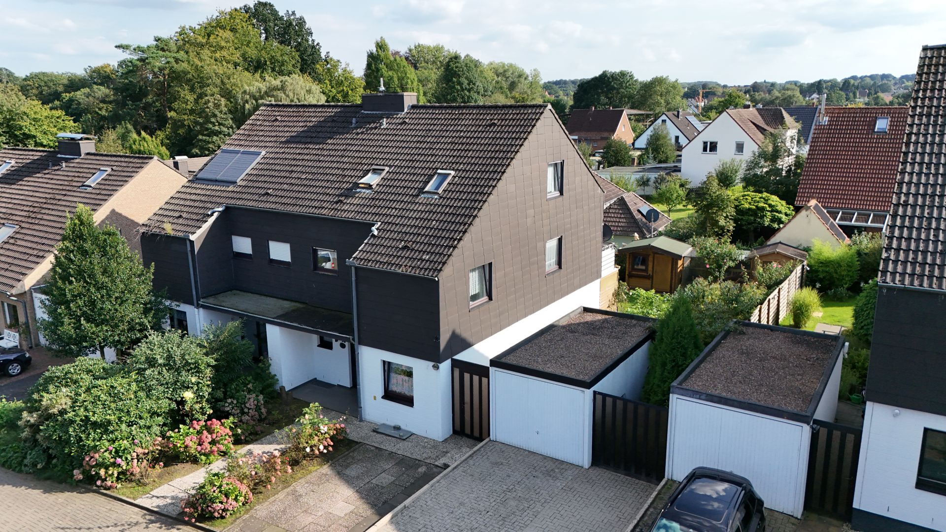 Modernes Reihenhaus mit Garten, Garagen und bepflanztem Vorgarten in einer ruhigen Wohnsiedlung.