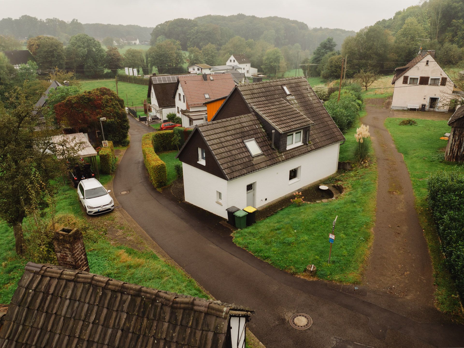 Blick auf mehrere Einfamilienhäuser mit Gärten und einer Straße in grüner, ländlicher Umgebung.