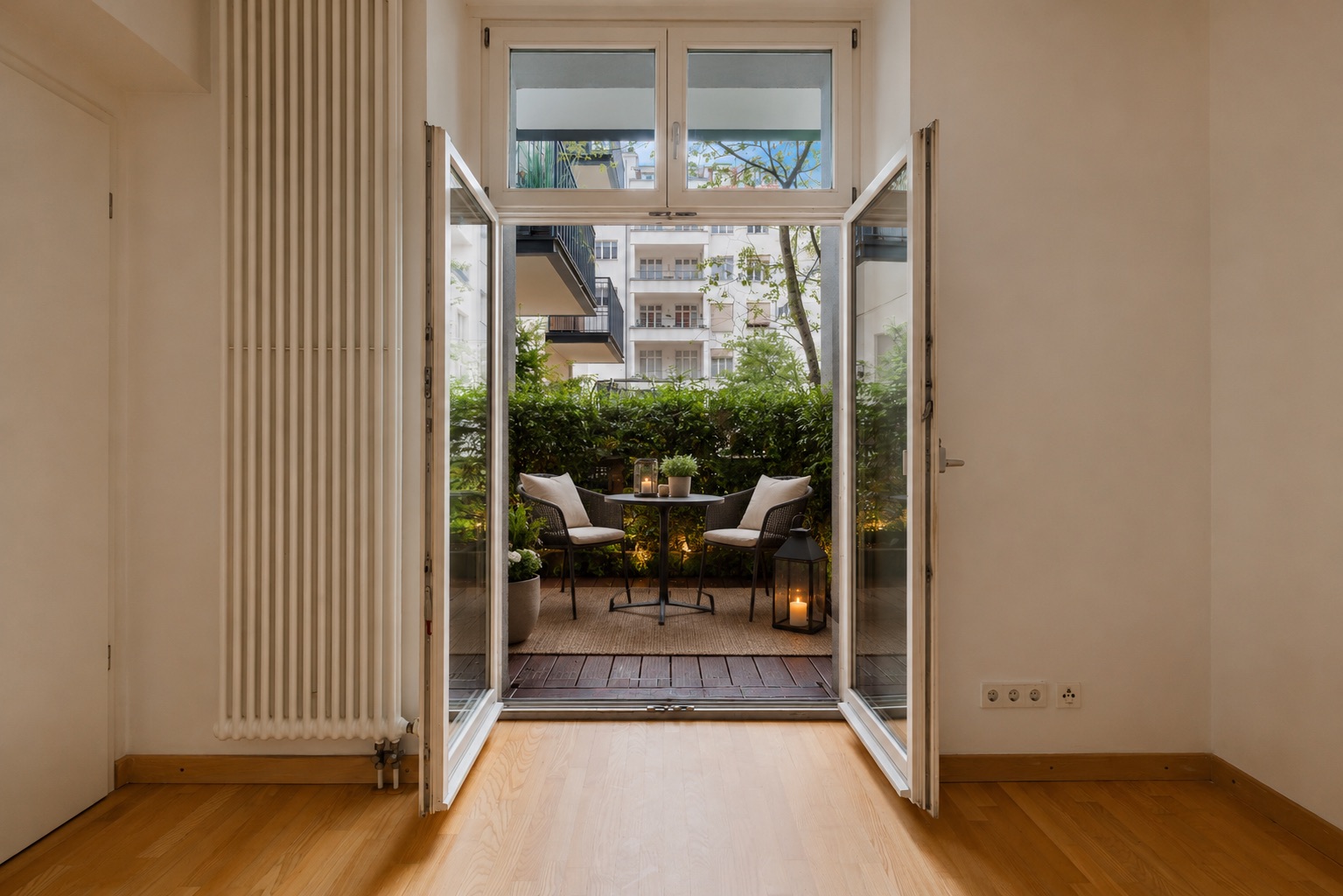 Blick durch offene Glastüren auf einen kleinen Balkon mit zwei Stühlen und einem Tisch.