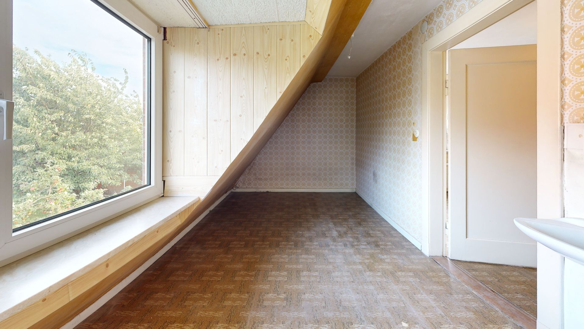 Heller Raum mit großem Fenster, Holzvertäfelung und schräger Decke.