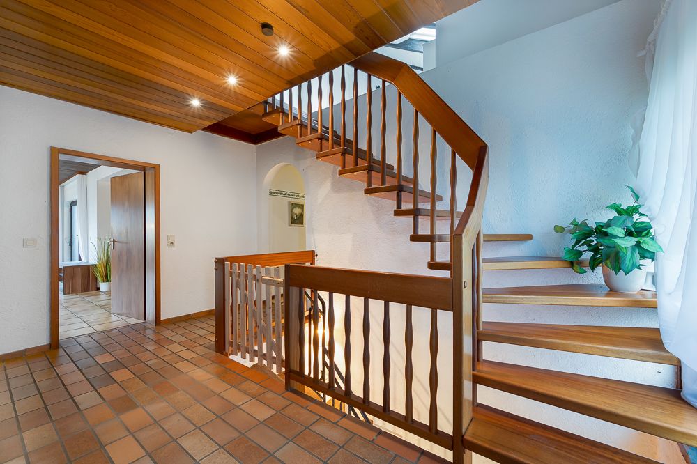 Treppenhaus mit Holztreppe, Fliesenboden und Pflanze auf dem Treppenabsatz.