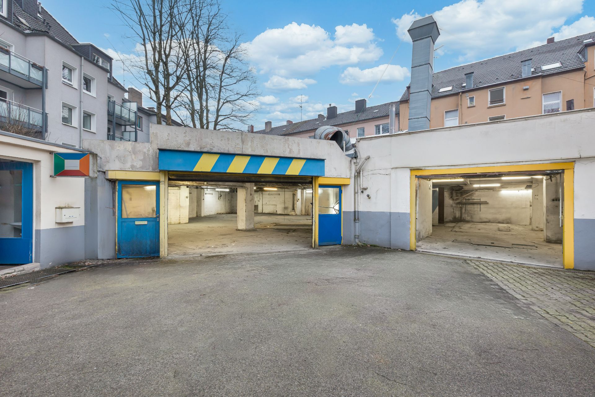 Offene Garagen mit blau-gelben Toren in einem Innenhof, dahinter Wohngebäude.