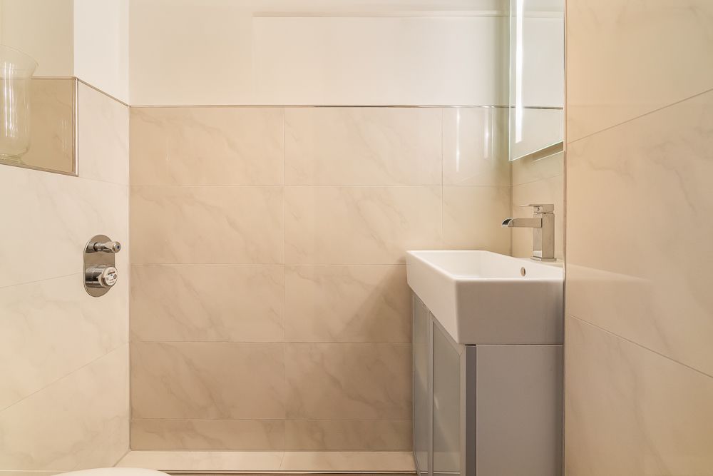 Modernes Badezimmer mit kleinem Waschbecken, Spiegel und beigen Fliesen.