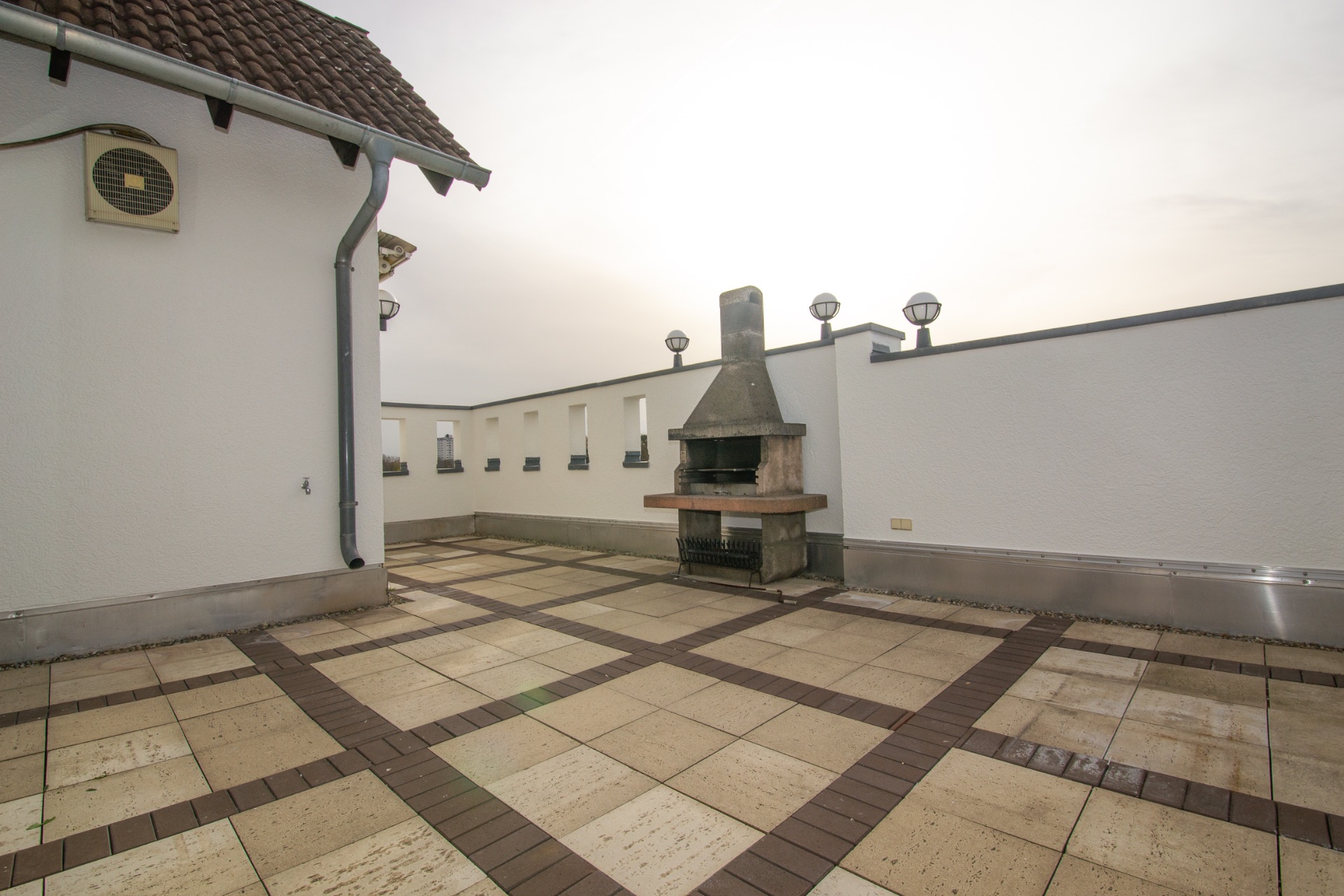 Große geflieste Dachterrasse mit gemauertem Grill und weißen Wänden.