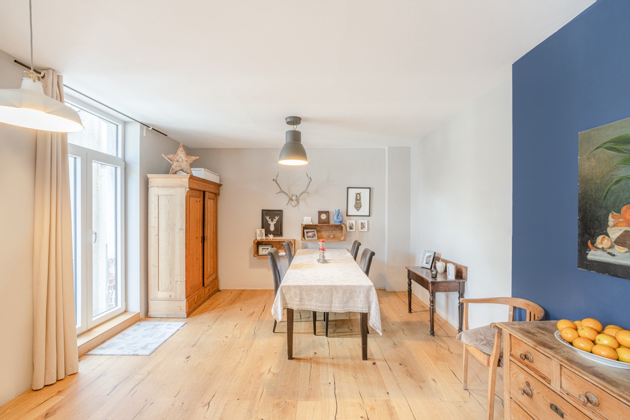 Heller Essbereich mit Holzboden, Tisch, Schrank und Dekoration an den Wänden.