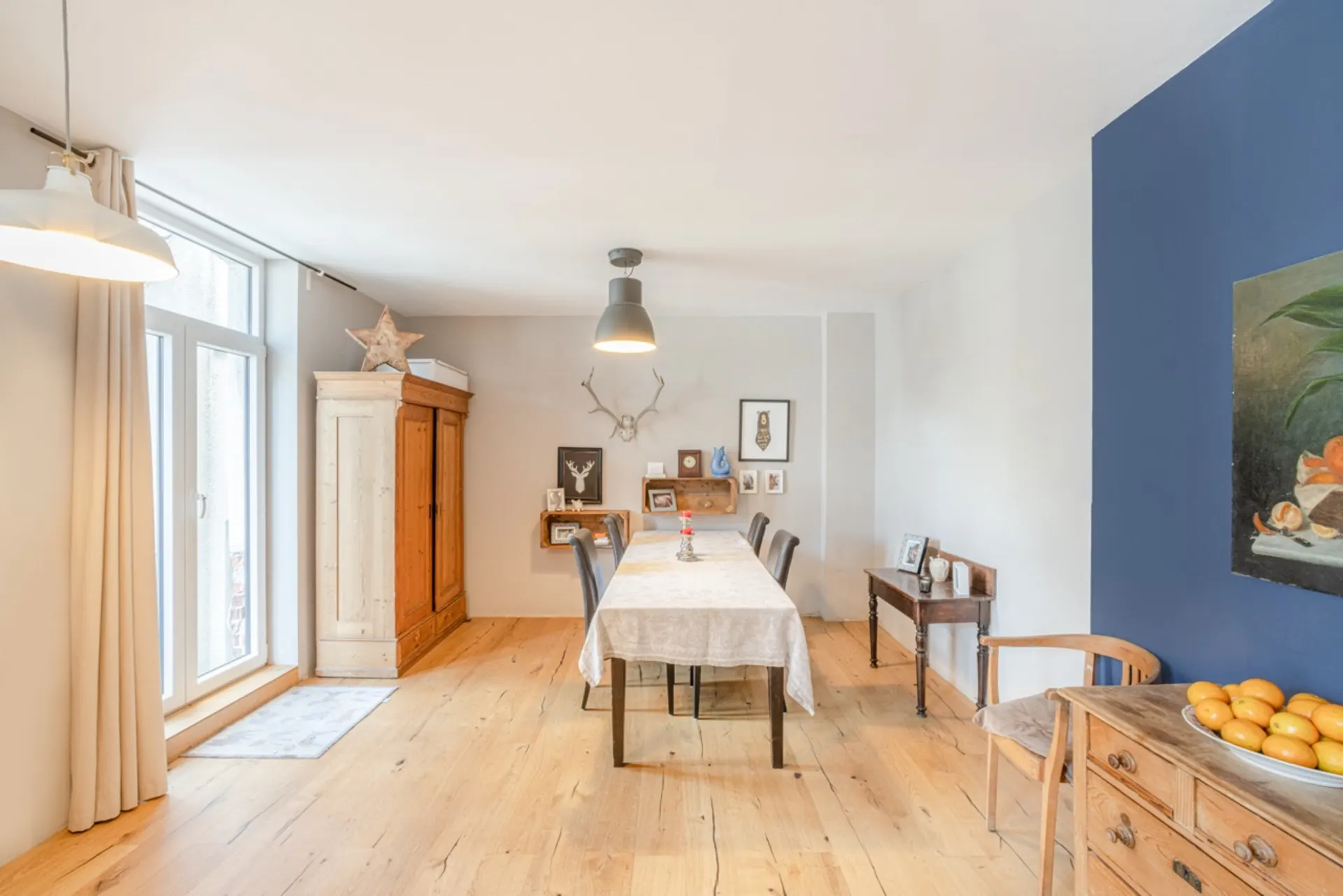 Heller Essbereich mit Holzboden, Tisch, Schrank und Dekoration an den Wänden.