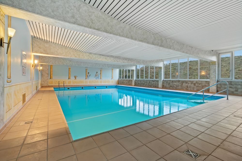 Helles Hallenbad mit großen Fenstern, Fliesenboden und Wanddekor.
