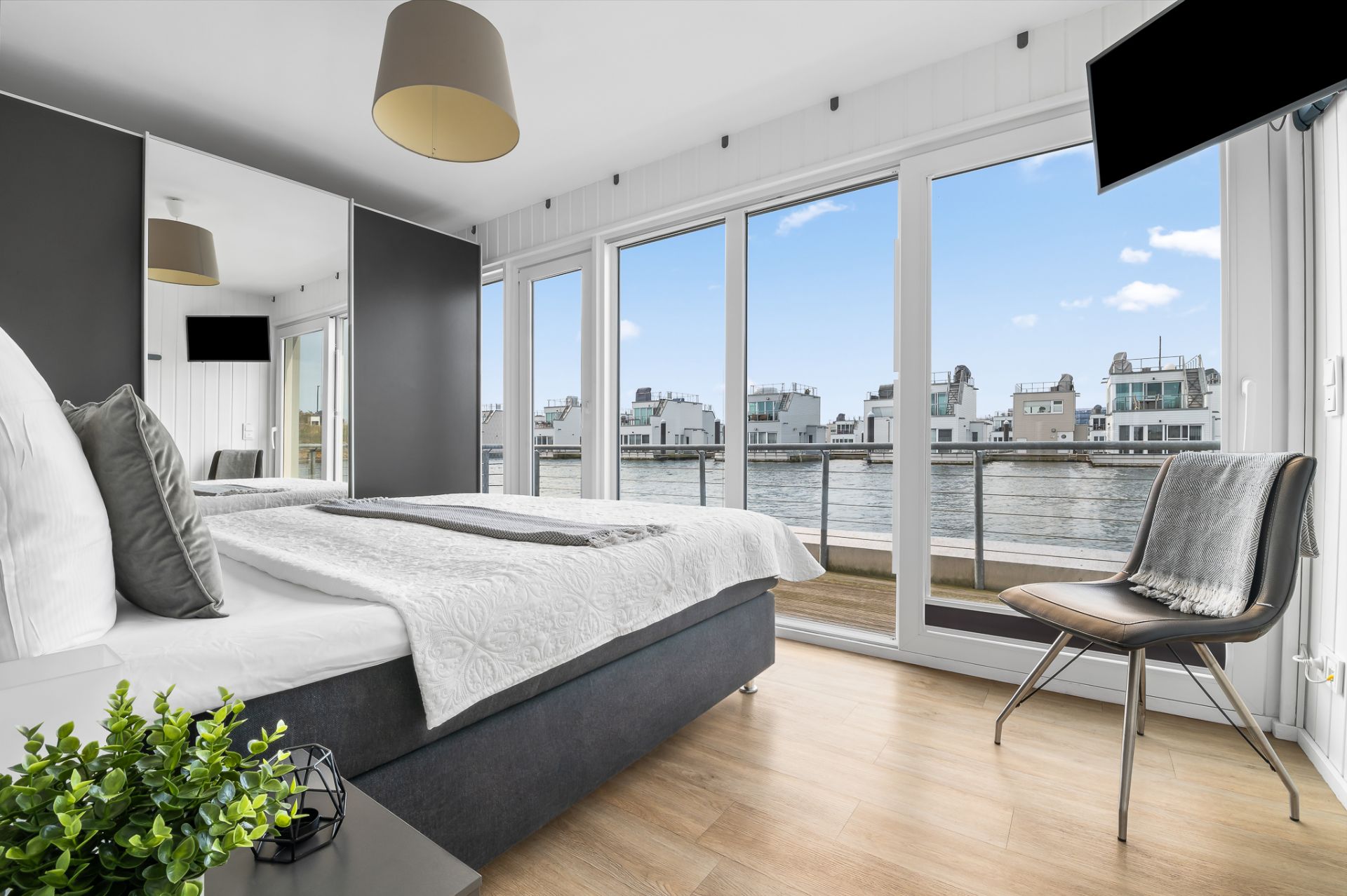 Modernes Schlafzimmer mit großem Bett, Stuhl und bodentiefen Fenstern mit Blick aufs Wasser.