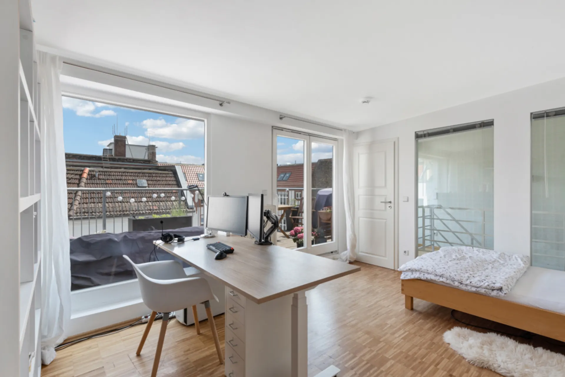 Helles Schlafzimmer mit Schreibtisch, Bett und Zugang zum Balkon, Holzboden und Dachfenster.