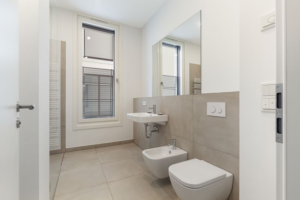 Modernes, helles Badezimmer mit großem Fenster, Waschbecken, Bidet und Toilette.