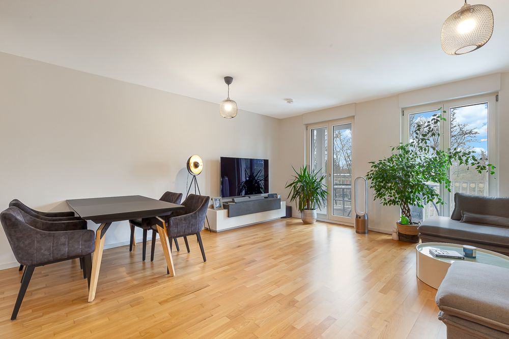 Modernes Wohnzimmer mit Esstisch, Fernseher, Sofa, großen Fenstern und Zimmerpflanzen.