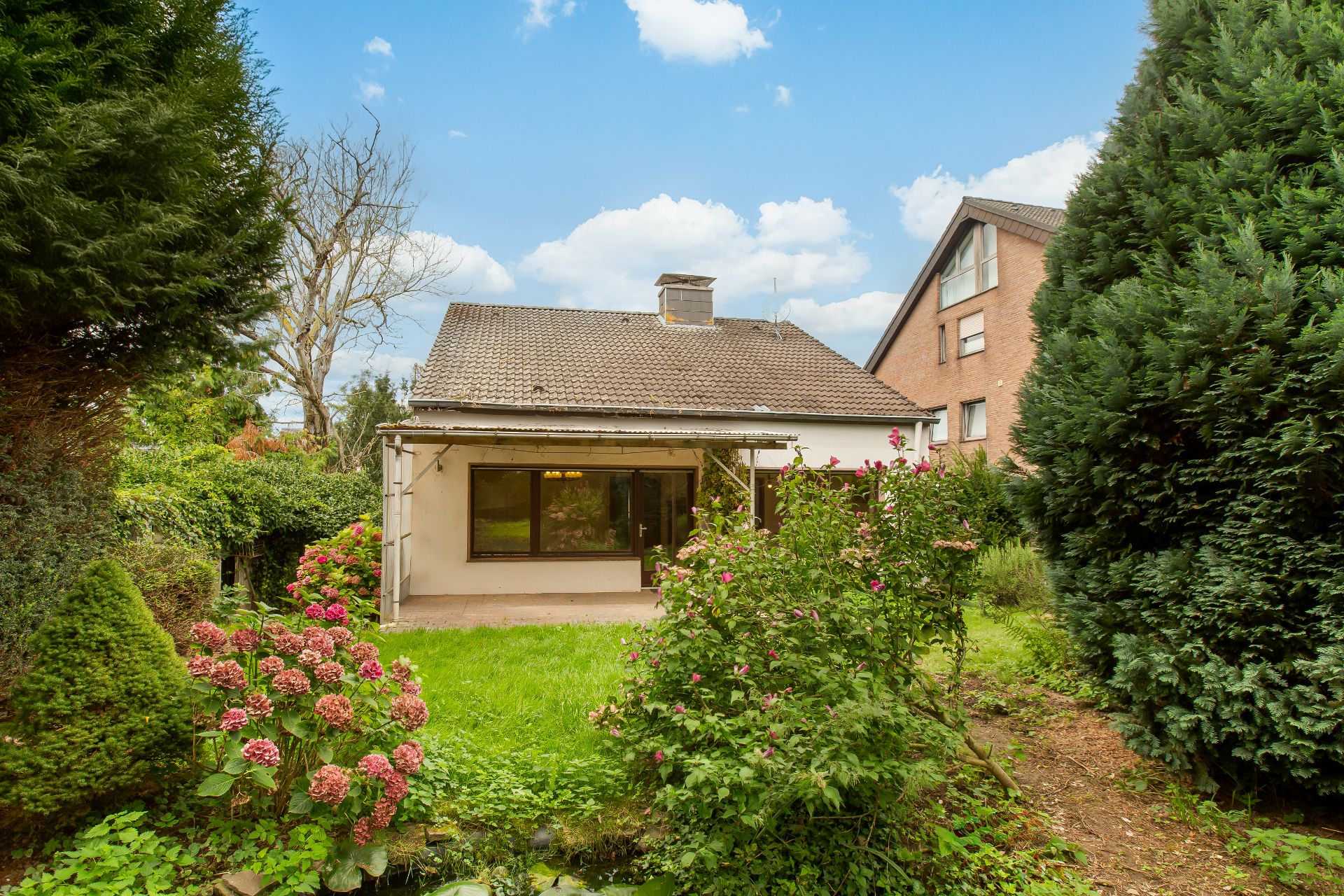 Blick auf ein Einfamilienhaus mit Garten, Sträuchern und Blumen im Vordergrund.