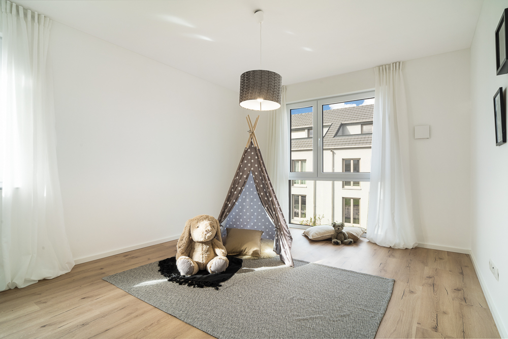 Helles Kinderzimmer mit Tipi-Zelt, Kissen, Kuscheltier und großem Fenster.