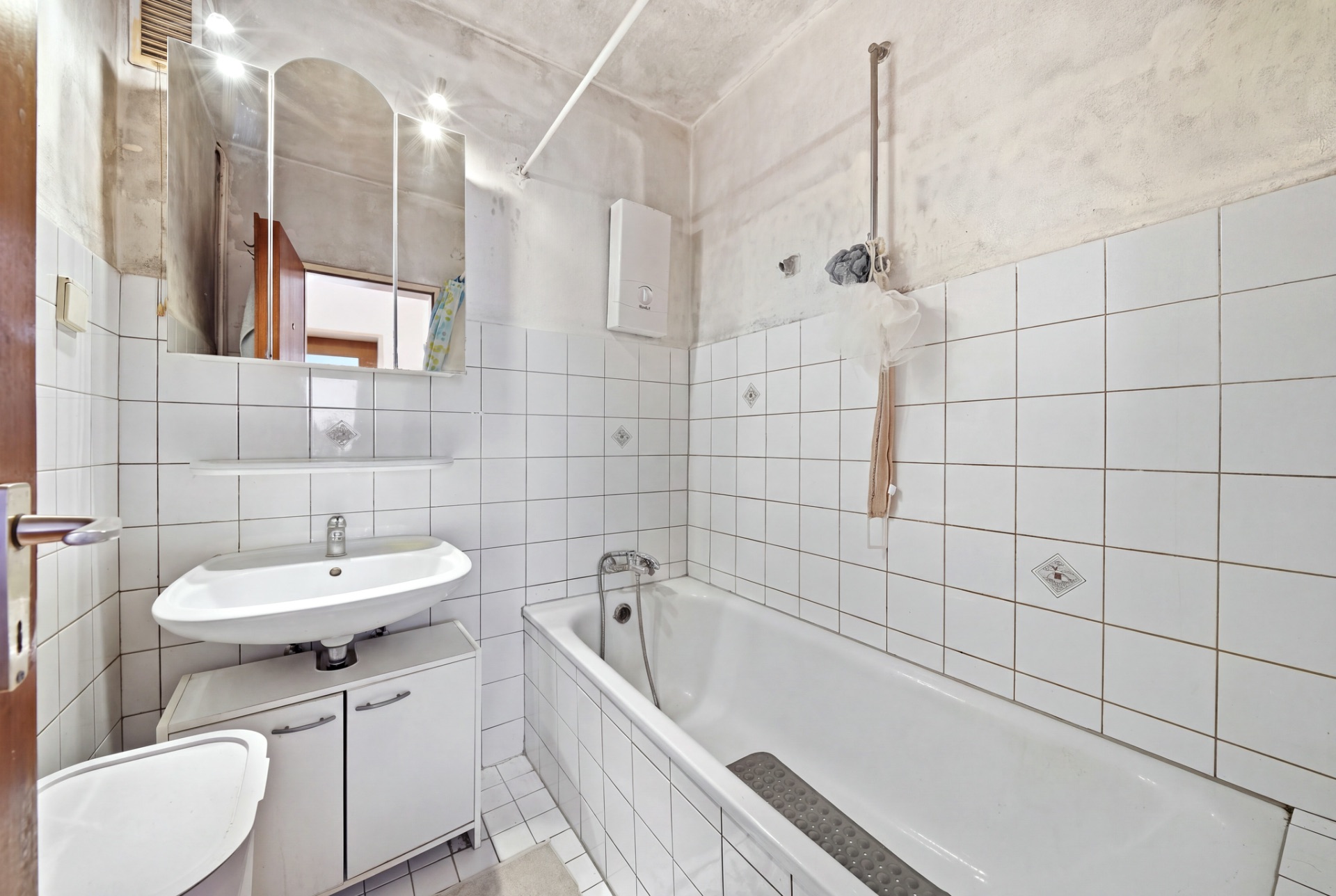 Kleines Badezimmer mit Badewanne, Waschbecken, Spiegel und weißen Fliesen.