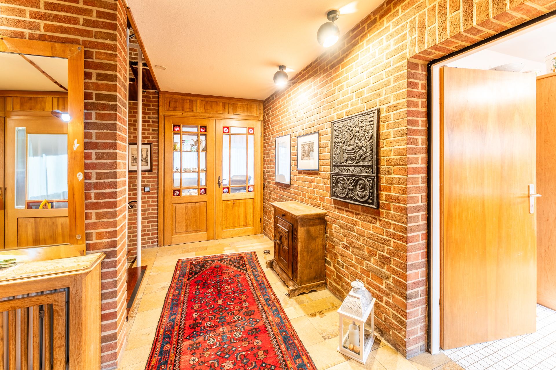 Heller Flur mit Backsteinwänden, rotem Teppich, Holztüren und Dekorationen an der Wand.