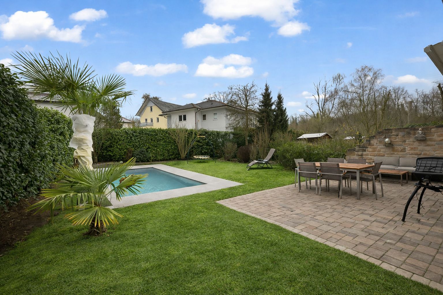 Garten mit Pool, Terrasse, Essbereich und Liegestühlen auf Rasen und Steinplatten.