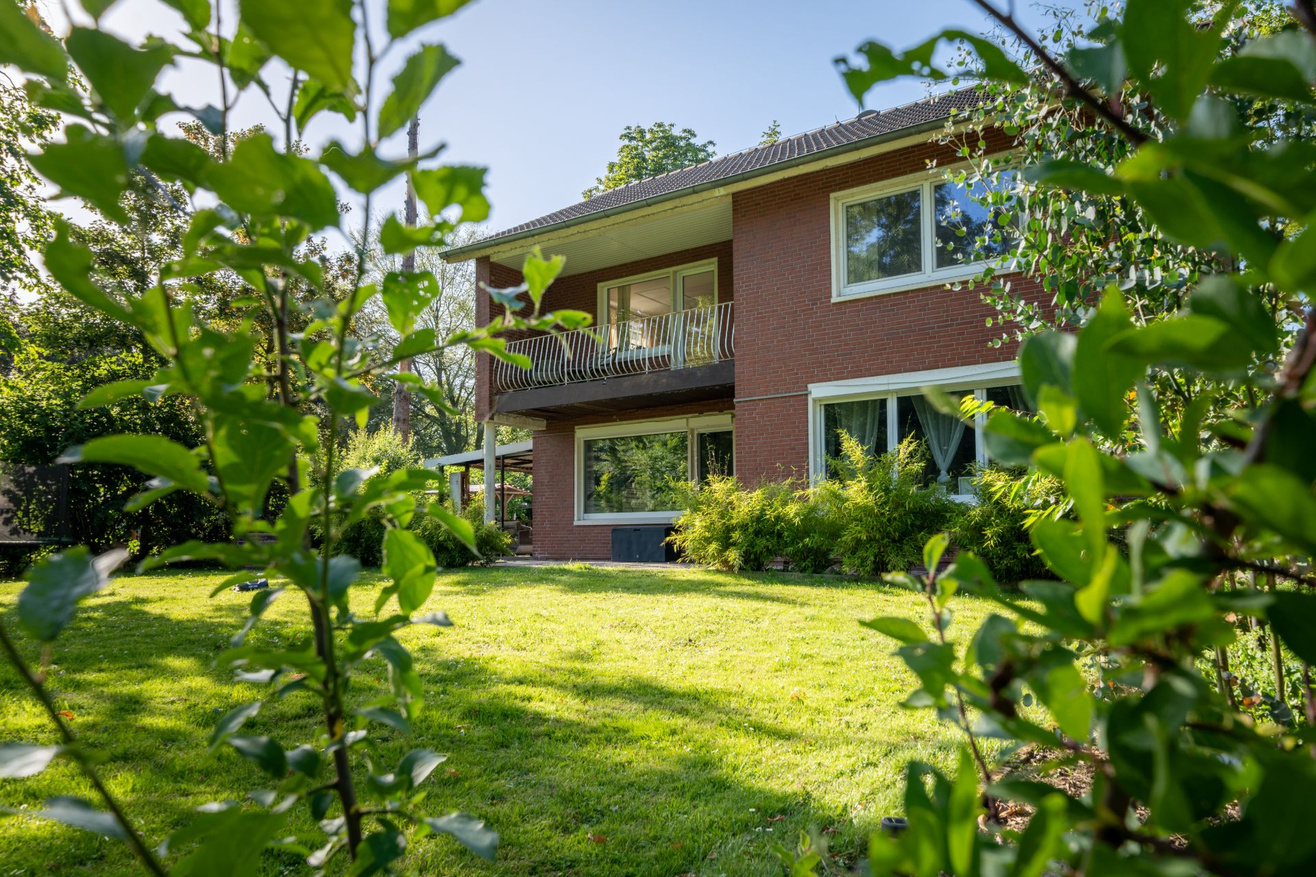 Zweistöckiges Haus mit Balkon und großem Garten, umgeben von Grünpflanzen.
