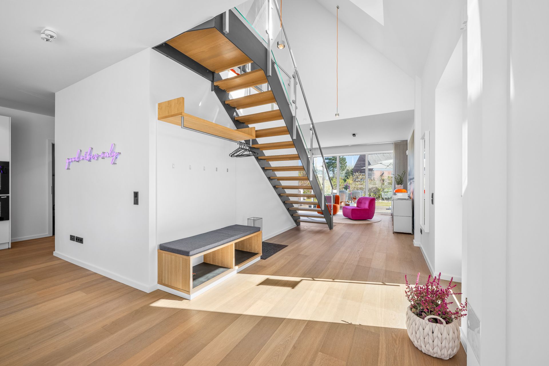 Heller Flur mit Holztreppe, Sitzbank und offener Blick ins Wohnzimmer mit großen Fenstern.