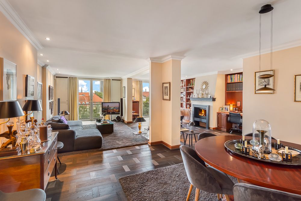 Modernes Wohnzimmer mit Sofa, Esstisch, Kamin, Schreibtisch und großen Fenstern mit Blick nach draußen.