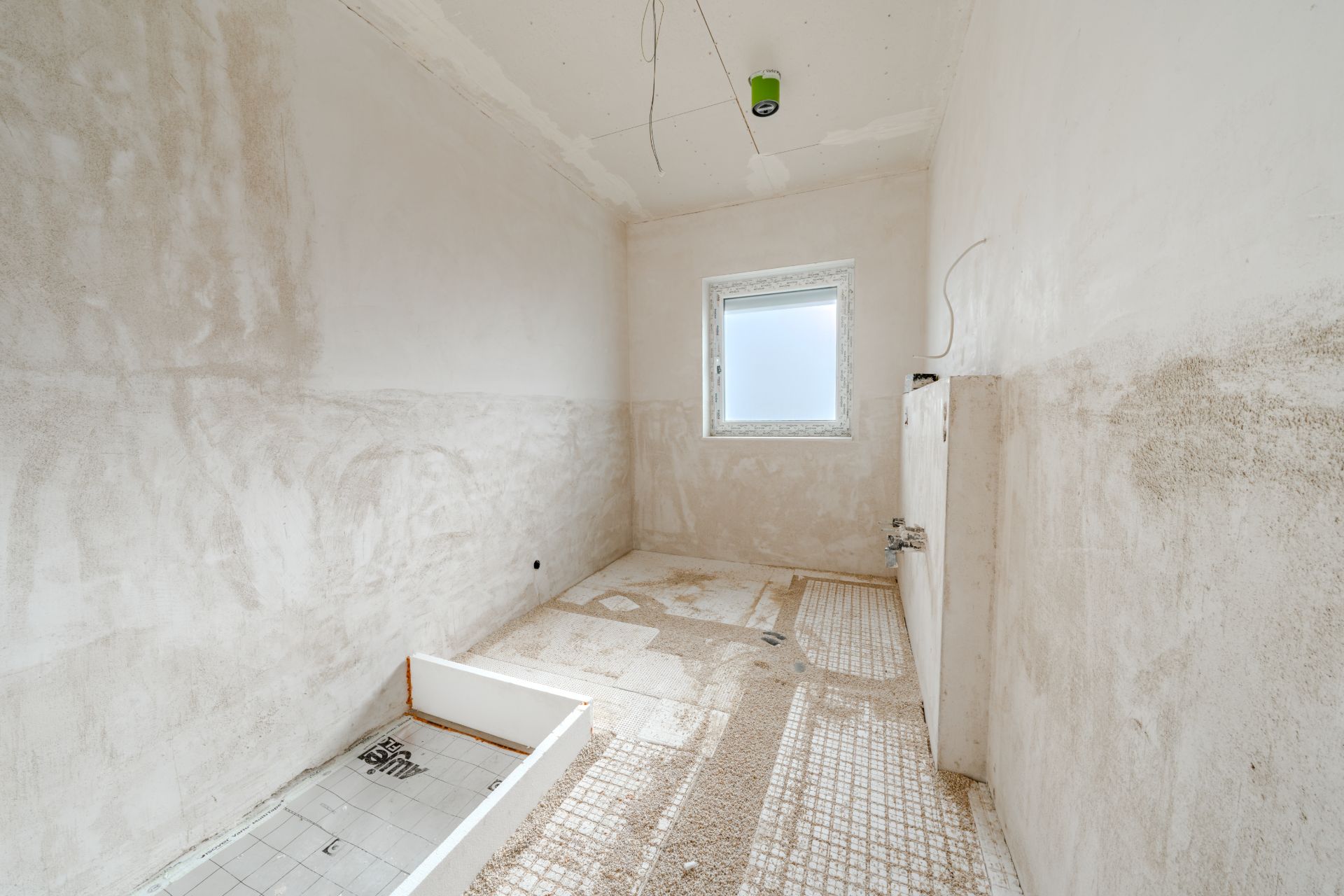 Unfertiges Badezimmer mit Fenster, Rohwänden und offener Dusche.