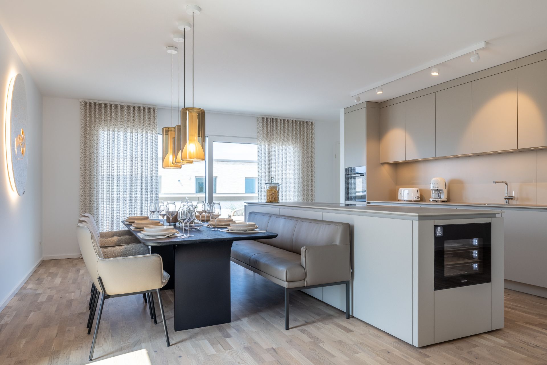 Moderne Küche mit Esstisch, Stühlen und Eckbank, helle Fenster und Holzfußboden.