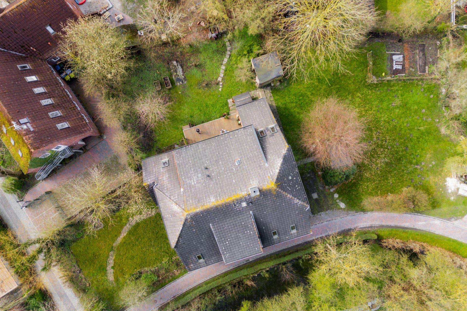 Luftaufnahme eines Wohnhauses mit Garten, Gehweg und umliegenden Bäumen.