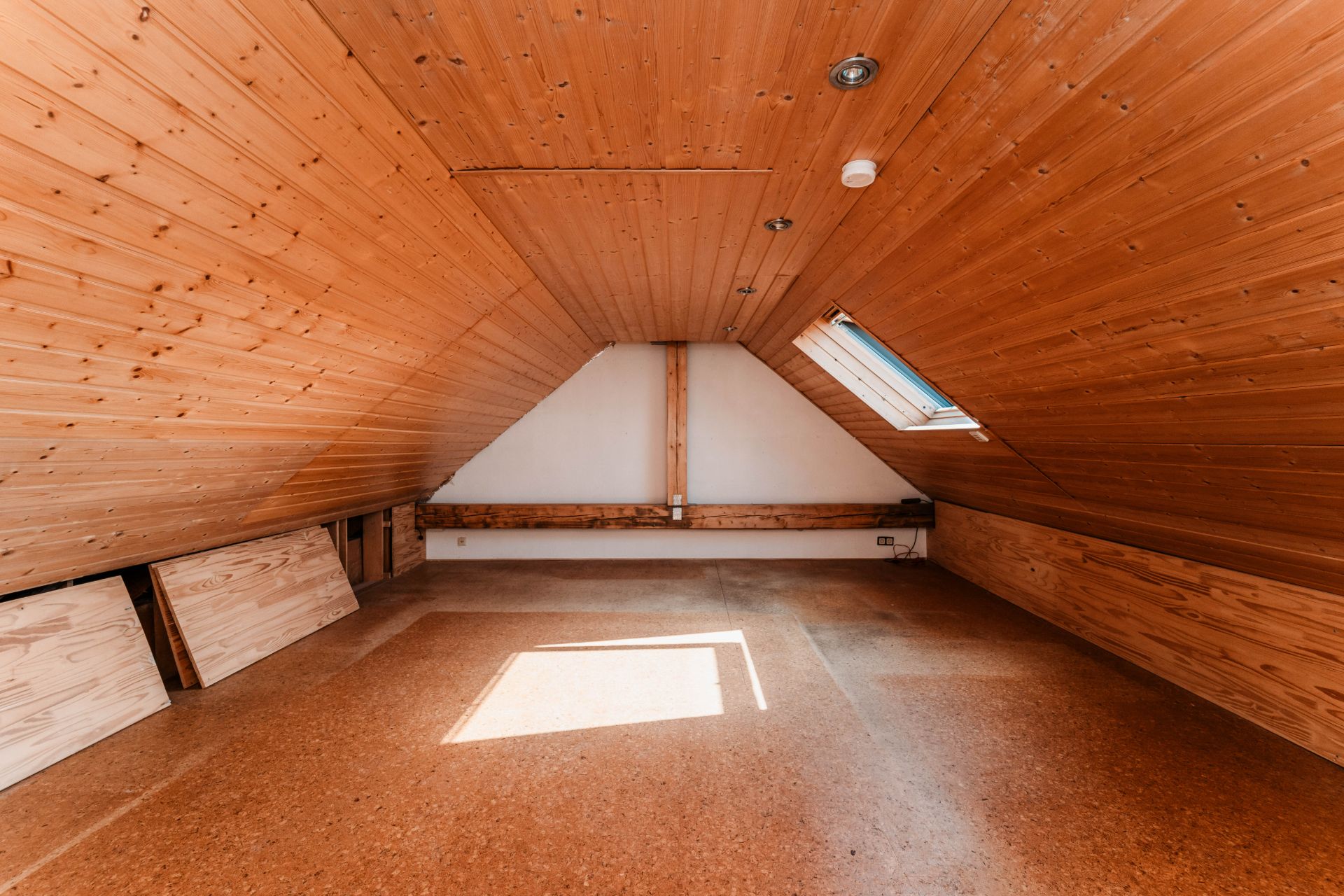 Dachbodenraum mit Holzverkleidung, Dachfenster und schräger Decke, Sonnenlicht fällt auf den Boden.