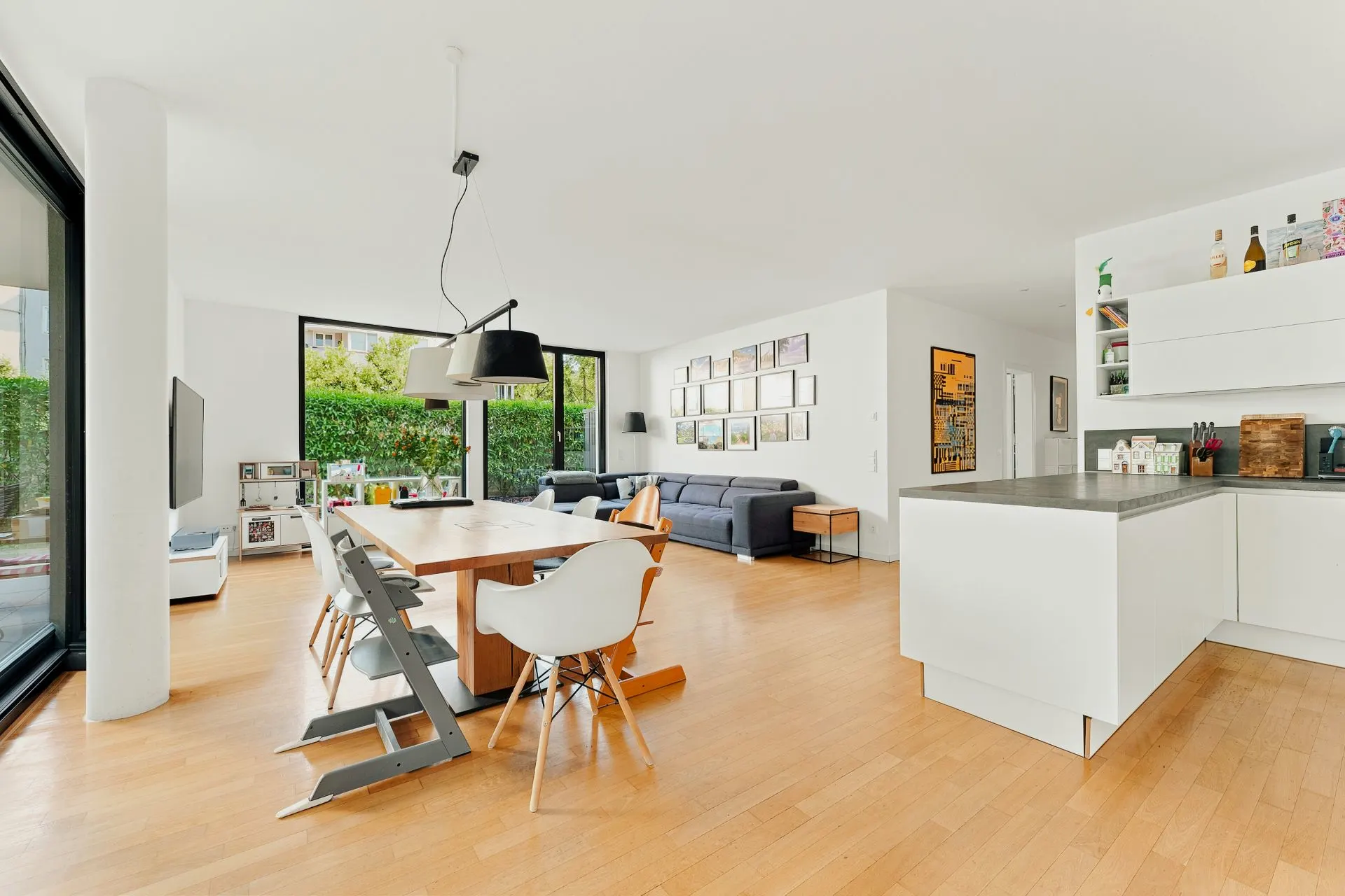 Helles Wohnzimmer mit Essbereich, moderner Küche und großen Fenstern auf Parkettboden.