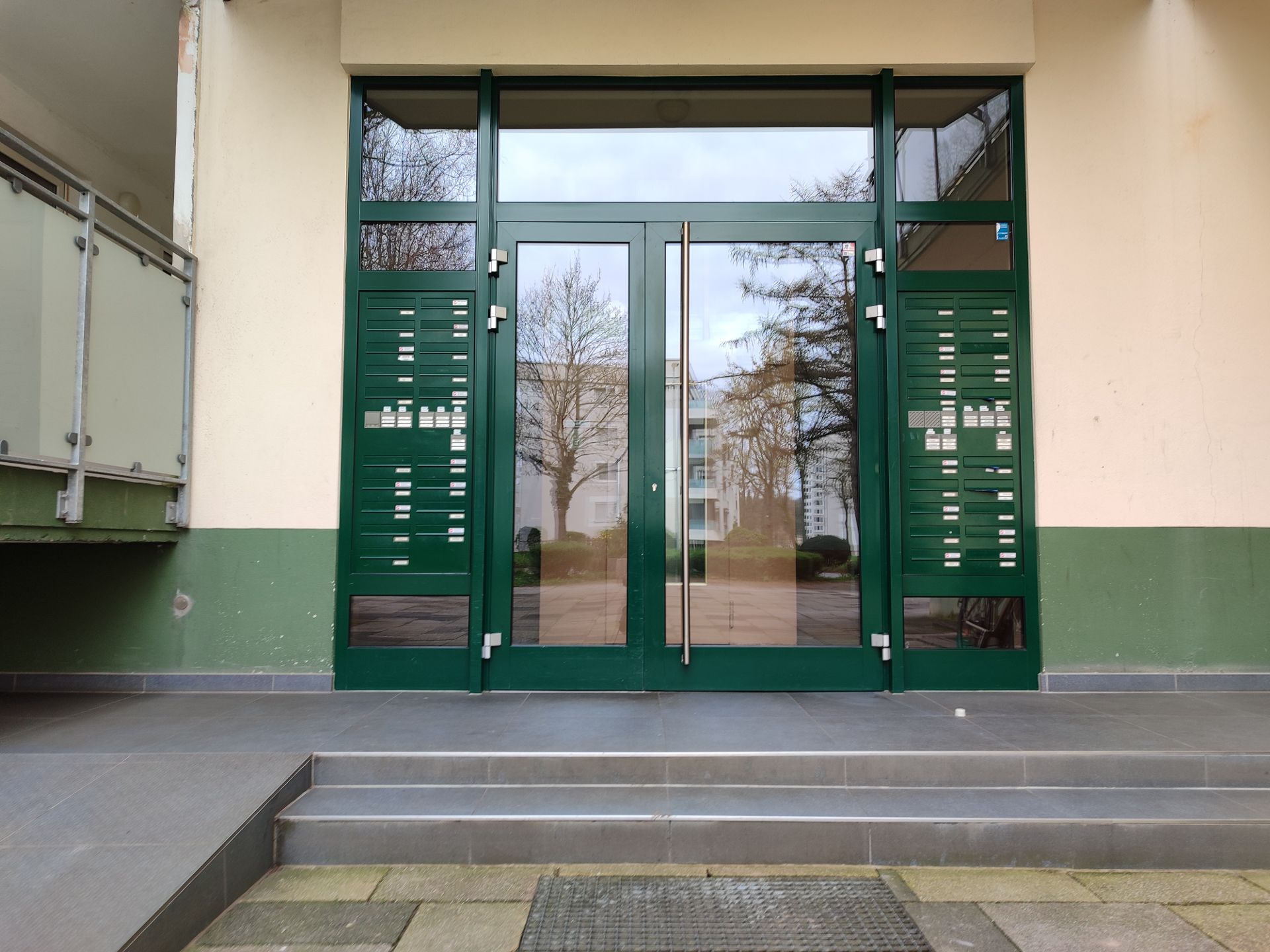 Eingangstür eines Wohnhauses mit Briefkästen und Glasfront, davor Treppenstufen.