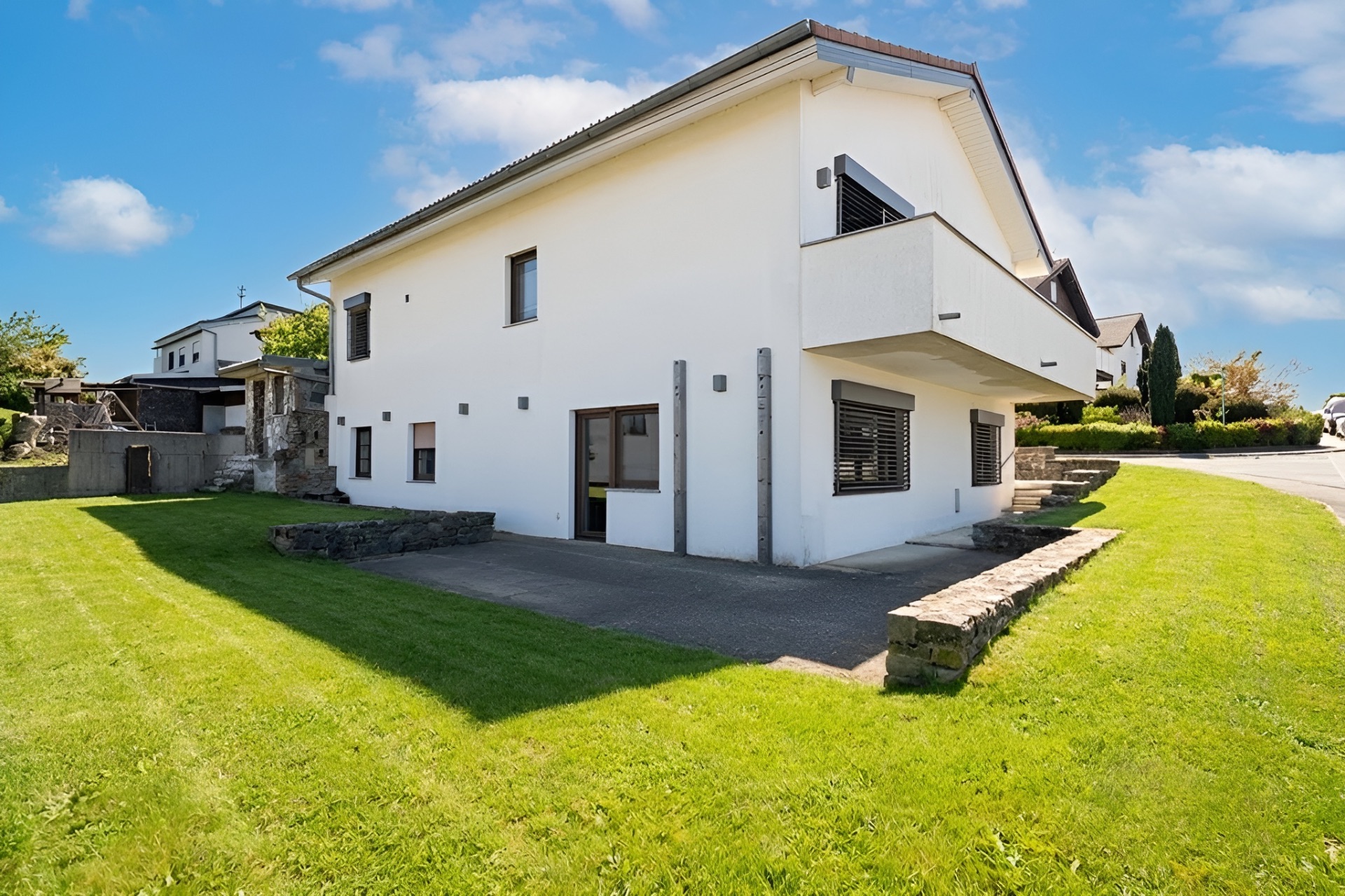 Modernes weißes Wohnhaus mit Balkon, großen Fenstern und gepflegtem Rasen.