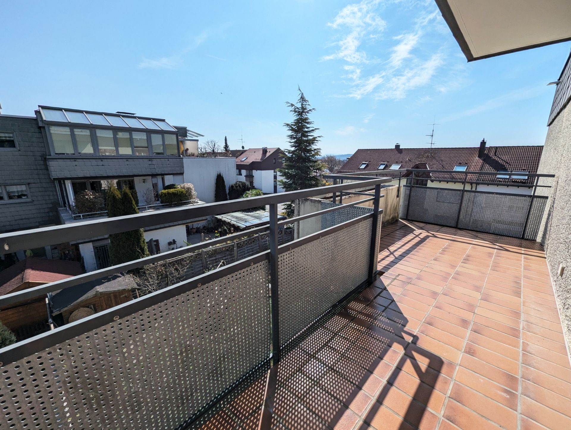 Großer Balkon mit Fliesenboden und Metallgeländer, Blick auf Nachbarhäuser und blauen Himmel.