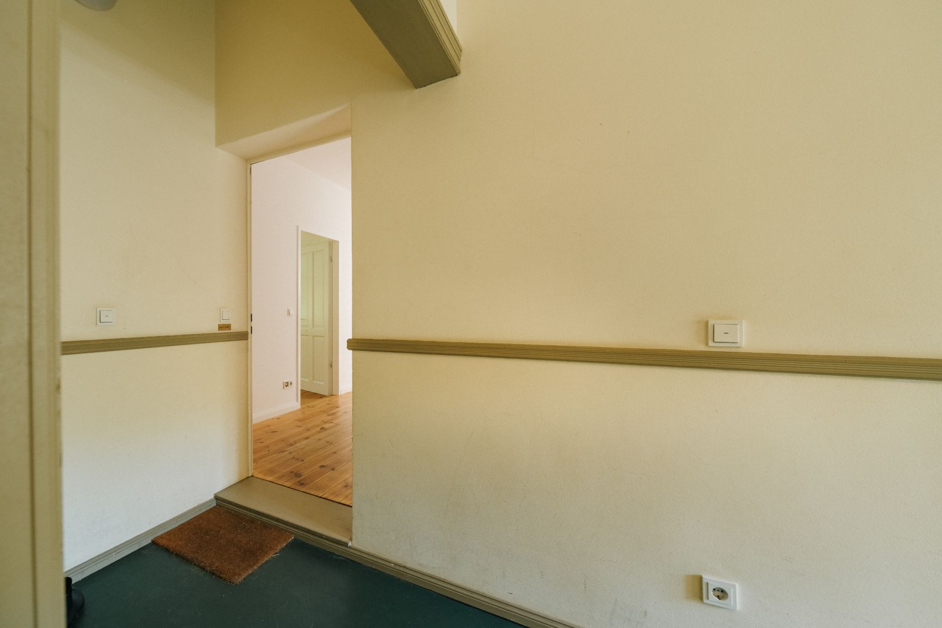 Flur mit beige gestrichenen Wänden, Türöffnung zu einem Raum mit Holzboden.