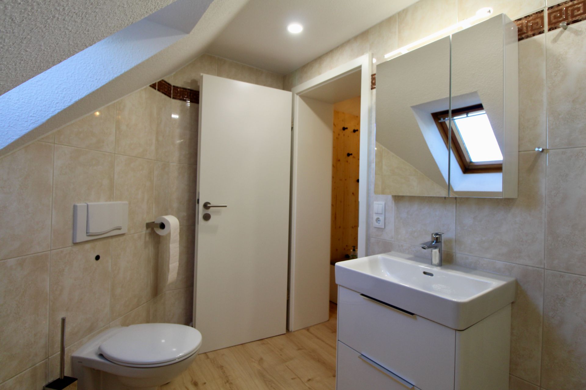 Modernes Badezimmer mit Toilette, Waschbecken, Spiegel und Dachfenster unter einer Schräge.