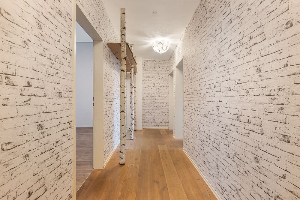 Heller Flur mit weißen Backsteinwänden und Holzboden, dekoriert mit Birkenstämmen.