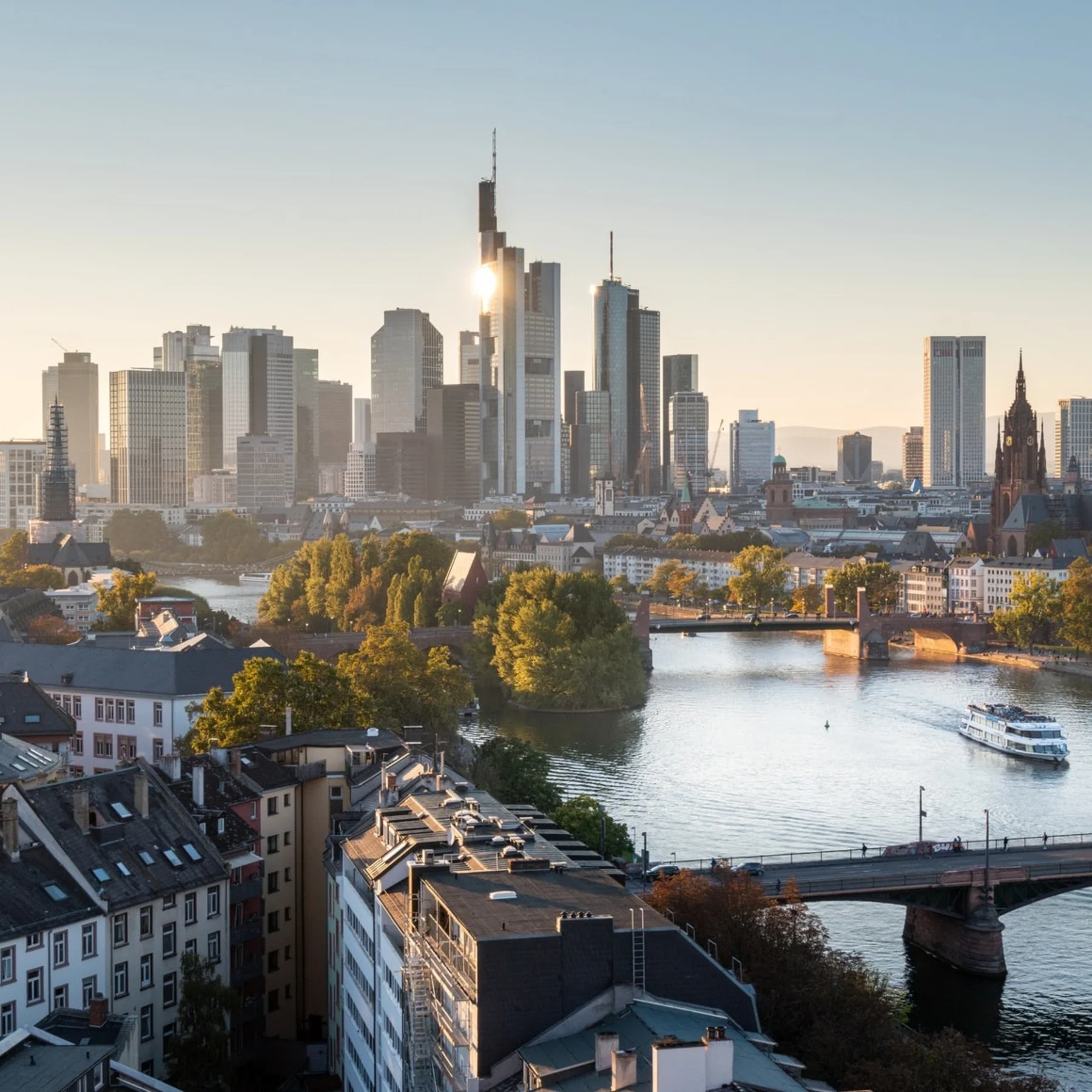 Stadtansicht mit Fluss, Brücke, Wohnhäusern und modernen Hochhäusern im Hintergrund.