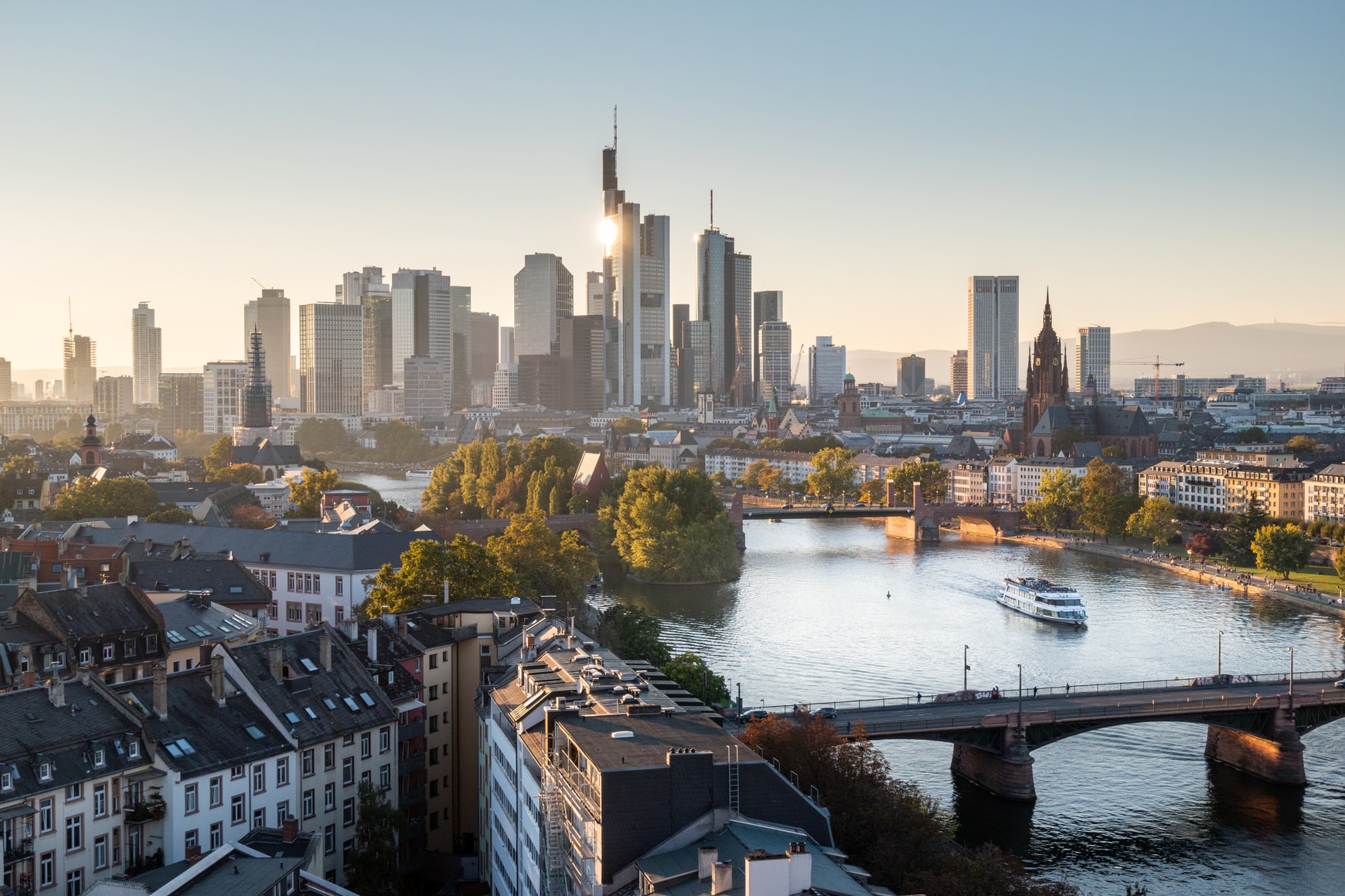 Stadtansicht mit Fluss, Brücke, Wohnhäusern und modernen Hochhäusern im Hintergrund.